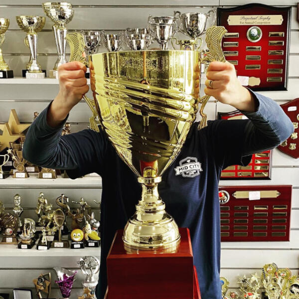 Mid City Gift & Trophy Centre staff member holding up large cup trophy in Geelong strore